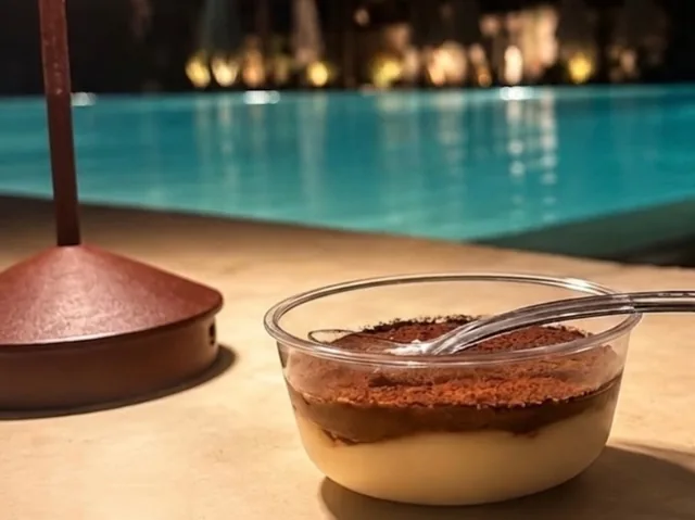 A cup of tiramisu with a spoon beside a glowing pool at night